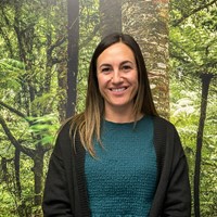 A woman smiling in front of a green forest. 