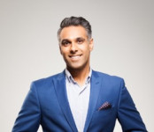 Arrun, a man with Gujarati heritage, has short grey hair. He is wearing a blue shirt, blue suit jacket and checkered pocket square