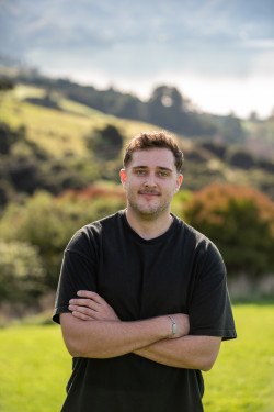 Josh McMillan is standing with his arms crossed in an outdoors setting