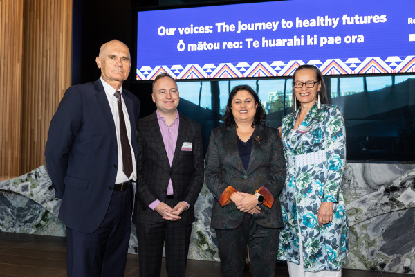 Left to right: Dr Peter Jansen, Deon York, Angie Smith, Hon Dr Ayesha Verrall. They are standing smiling happily in front of the reception desk at Te Pae. The digital sign in the background says ‘Our voices: The journey to healthy futures. Ō mātaou reo: Te huarahi ki pae ora’.
