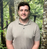 Josh has short dark hair and stubble. He is wearing a beige polo shirt