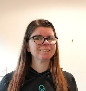 Photo of Kim. She has long brown hair, black eye glasses and is wearing a black top.