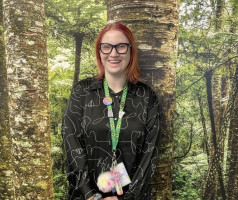 Natasha has straight shoulder length red hair and glasses. She is wearing a black dress with a white pattern