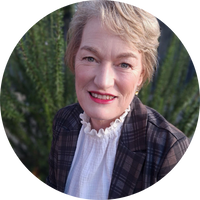 Clare has short blonde hair.  Clare is wearing red lipstick, a white blouse with a frilly neckline and a checkered blazer