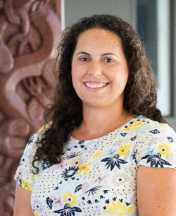 An image of Joana Hikaka. She has long dark hair and wears a light coloured top with flower imagery