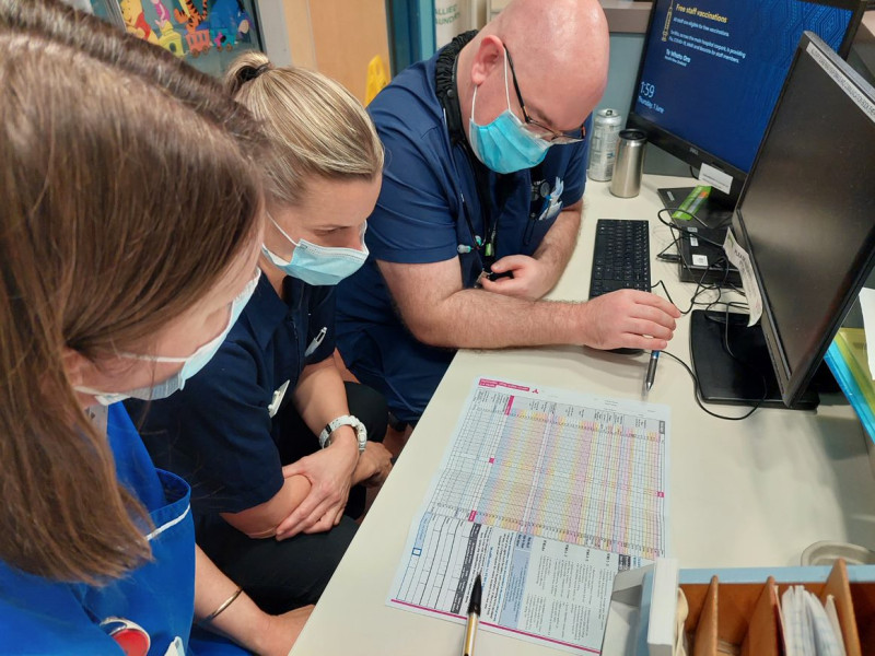 An image of three clinicians sitting at a desk looking at one of the revised paediatric vital signs chart.