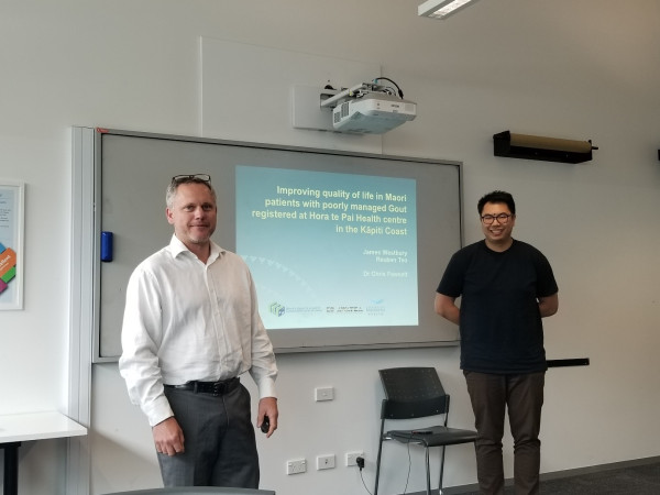 An image of James Westbury and Reuben Teo standing in front of a presentation titled 'Improving quality of life in Māori patients with poorly managed gout regisitered at Hora te Pai Health centre in the Kāpiti Coast'