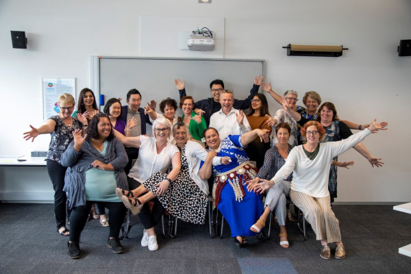 A group of graduates posing together and waving their hands in front of a whiteboard