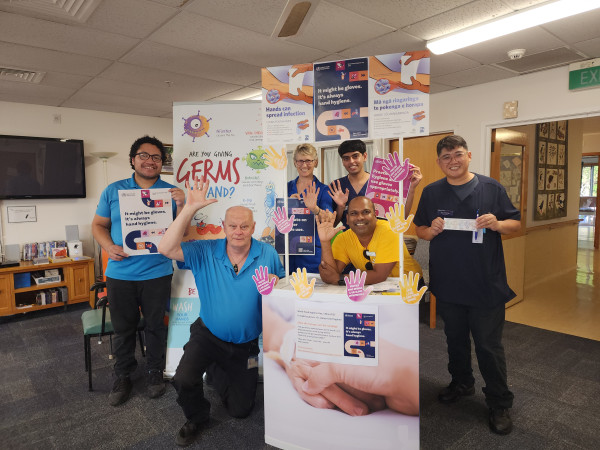 A group of people posing for a photo around a stand that has been decorated with hand hygiene posters and handprint cutouts.