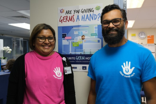 Two staff wearing hand hygiene t-shirts in front of wall display in Ward 16 Whangarei hospital.
