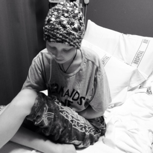 A black and white image of a child wearing a bandanna and sitting in a hospital bed.