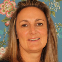 A head shot of Jo Wailing. She has long blonde hair and stands against a flowery wallpaper background.