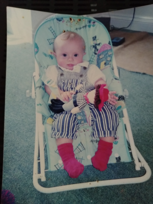 A picture of a baby with blonde hair sitting in a baby chair holding a toy cowboy